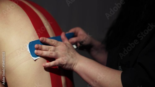 The masseur sticks teips on the back of a young woman photo