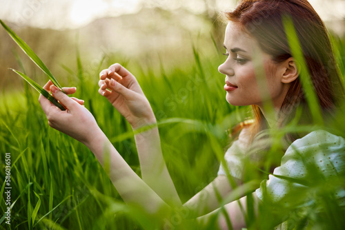 portrait of a blissfully smiling woman sitting in the grass with a leaf in her hand