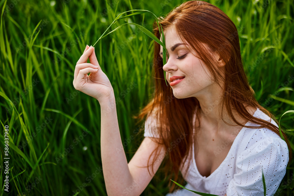 portrait of a cute red-haired woman sitting in tall grass and holding a leaf in her hands portrait of a cute red-haired woman sitting in tall grass and holding a leaf in her hands