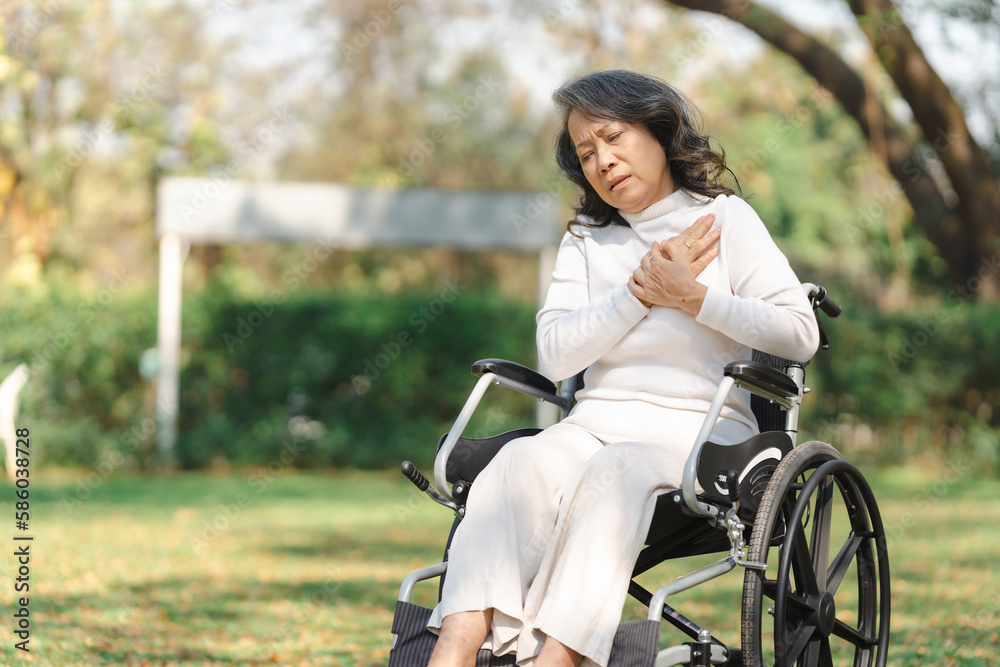 Asian old woman sitting on a wheelchair outdoors in the park There is pain in the heart and myocardium.