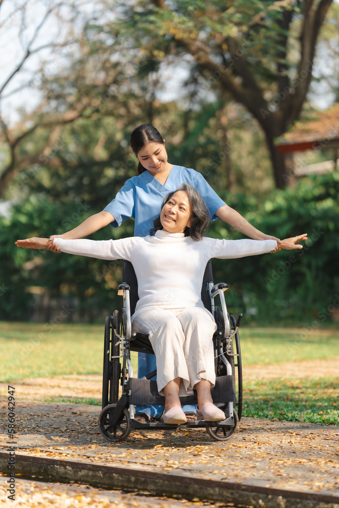 Young asian care helper with asia elderly woman on wheelchair relax together park outdoors to help and encourage and rest your mind with green nature. physical therapy