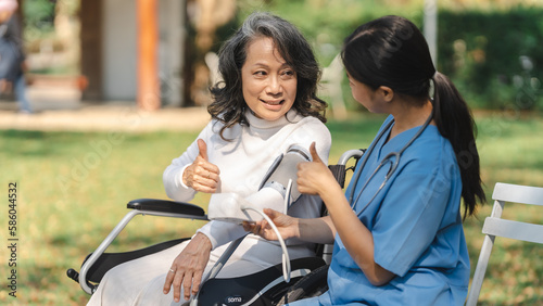 Young asian care helper with asia elderly woman on wheelchair relax together park outdoors to help and encourage and rest your mind with green nature. measure blood pressure