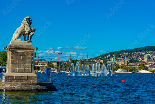 Panorama of Siwss town Zuerich behind a lion statue and Springbrunnen fountain photo
