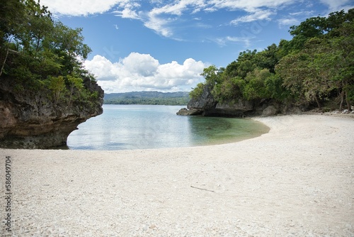 Idyllic, secluded beach of Siquijor in the Philippines with white sand and crystal clear water in a small bay with trees and cliffs.