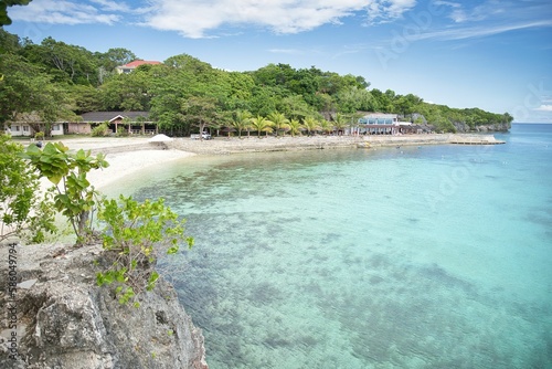 Idyllic  secluded beach of Siquijor in the Philippines with white sand and crystal clear water in a small bay with trees and cliffs.