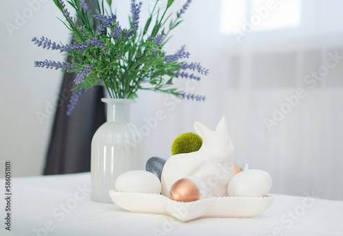 plate with Easter eggs, rabbits, lavender and napkin on white table. Concept of home comfort in bright Easter holiday