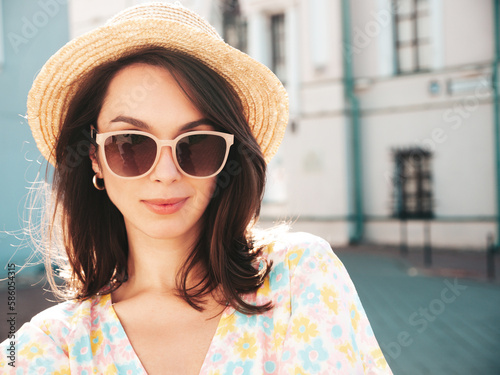 Beautiful smiling brunette model. Trendy female posing in the street background. Funny and positive woman having fun outdoors at sunset. In hat at sunny day. In dress and sunglasses