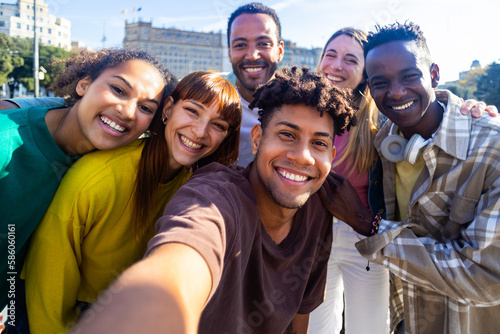 Multiethnic group of young best friends having fun together outdoors. Millennial happy men and women showing unity taking selfie portrait in city street. Community and friendship concept