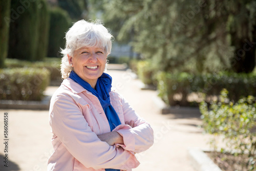 middle-aged woman with white hair smiling looking at camera with arms crossed in park
