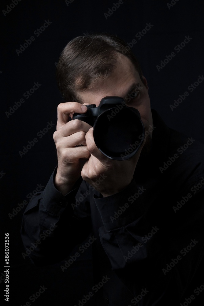 Low key portrait of a professional photographer man with a camera in the dark, look at camera, copy space.