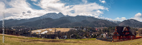 Panoramic view on Tatra Mountains seen from Koscielisko, Poland. Sunny day in early spring. Snow-covered peaks of the Tatras, melting snow in the mountain pastures. Traditional landscape from Podhale.