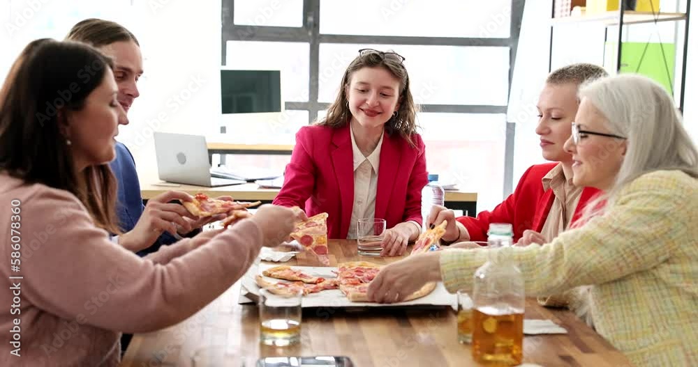 Delighted colleagues take slices of delicious pizza sitting at big wooden table in premise. Happy man and women enjoy lunch at work break in office slow motion Delighted colleagues take slices of delicious pizza sitting at big wooden table in premise. Happy man and women enjoy lunch at work break in office slow motion