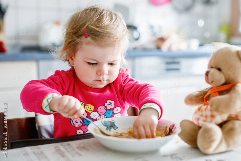 Adorable baby girl eating from fork vegetables and pasta. food, child, feeding and development concept. Cute toddler, daughter with spoon sitting in highchair and learning to eat by itself. Adorable baby girl eating from fork vegetables and pasta. food, child, feeding and development concept. Cute toddler, daughter with spoon sitting in highchair and learning to eat by itself.
