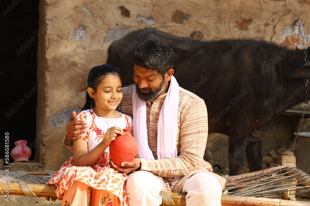 Happy rural Indian father and daughter sitting together on a cot ...