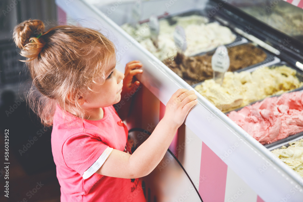 Cute little toddler girl choosing and buying ice cream in a cafe. Happy baby child looking at different sorts of icecream. Sweet home made dessert - obrazy, fototapety, plakaty 