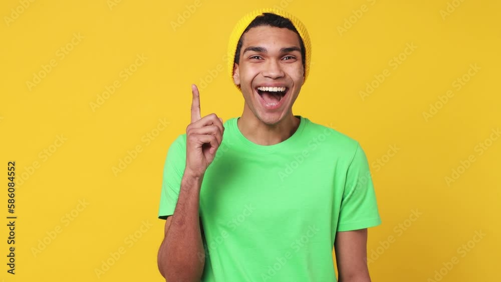 Excited insighted smart proactive pensive young man of African American ethnicity wear green t-shirt hat look around think comes up with idea raised finger get plan isolated on plain yellow background Excited insighted smart proactive pensive young man of African American ethnicity wear green t-shirt hat look around think comes up with idea raised finger get plan isolated on plain yellow background