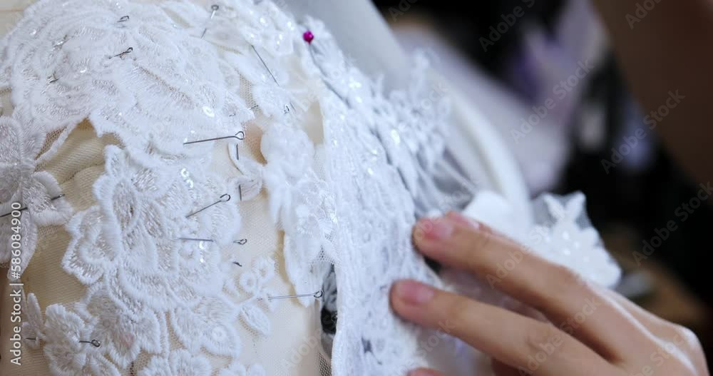 the female hand of a seamstress sticks pins into the corset details of a wedding dress on a mannequin. production of wedding dresses. close-up the female hand of a seamstress sticks pins into the corset details of a wedding dress on a mannequin. production of wedding dresses. close-up