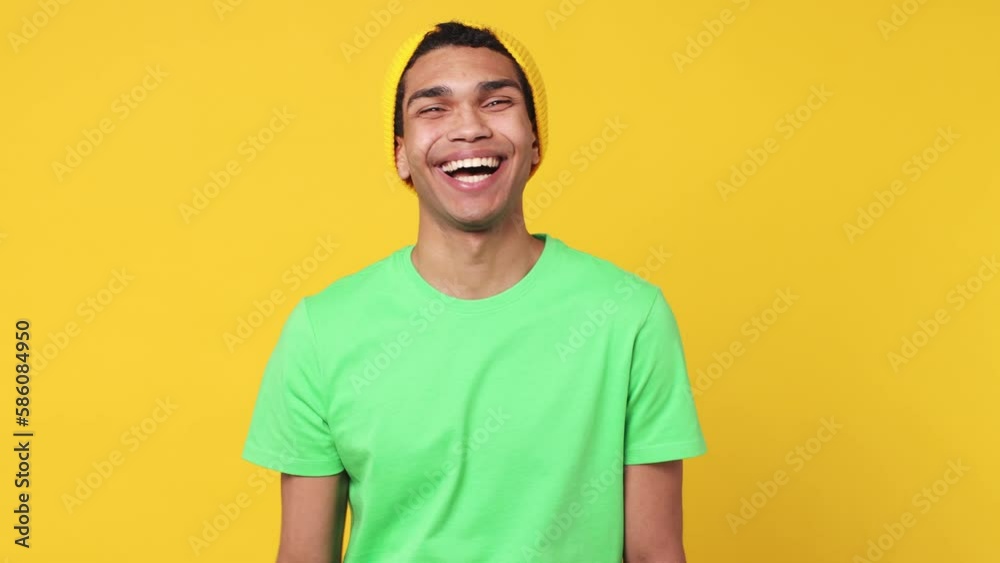 Young fun man of African American ethnicity wear green t-shirt hat point finger camera on you doing phone gesture like says call me back blinking isolated on plain yellow background studio portrait Young fun man of African American ethnicity wear green t-shirt hat point finger camera on you doing phone gesture like says call me back blinking isolated on plain yellow background studio portrait