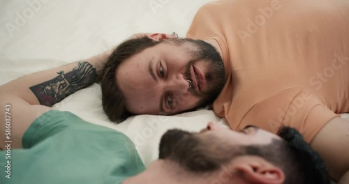 Portrait of attractive bearded gay men couples laying on bed together, talking photo
