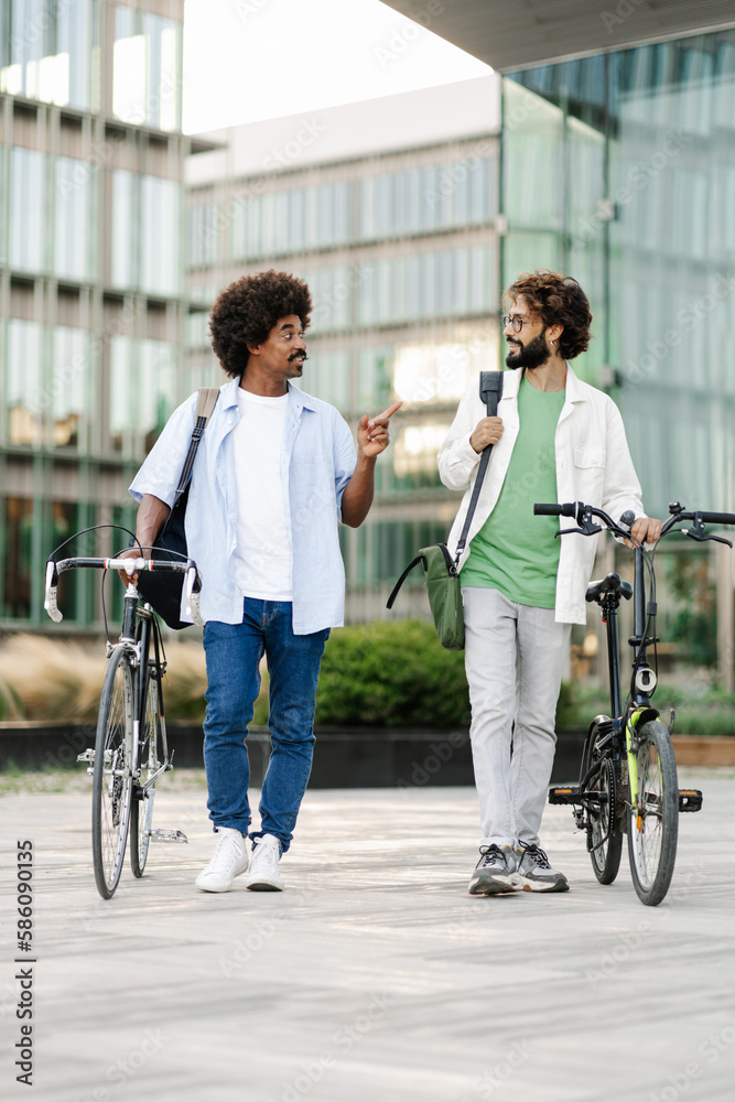 Two young male friends with bicycle - Modern coworkers walking outside office Two young male friends with bicycle - Modern coworkers walking outside office