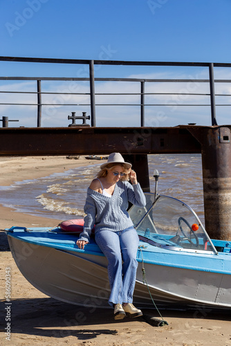 Portrait of a young beautiful girl in a blue sweater and jeans is on a boat near the river pier

