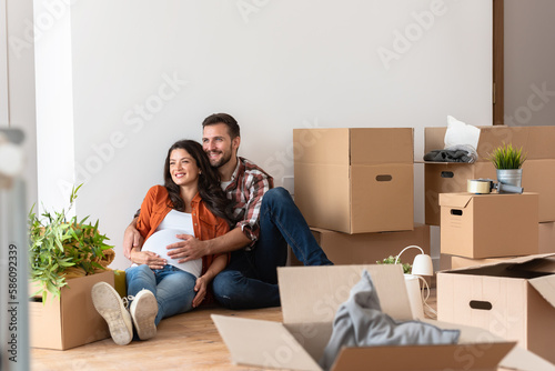 Beautiful young couple expecting a baby just moved into an empty apartment, sitting among cardboard boxes making plans for the future. New beginnings © lordn