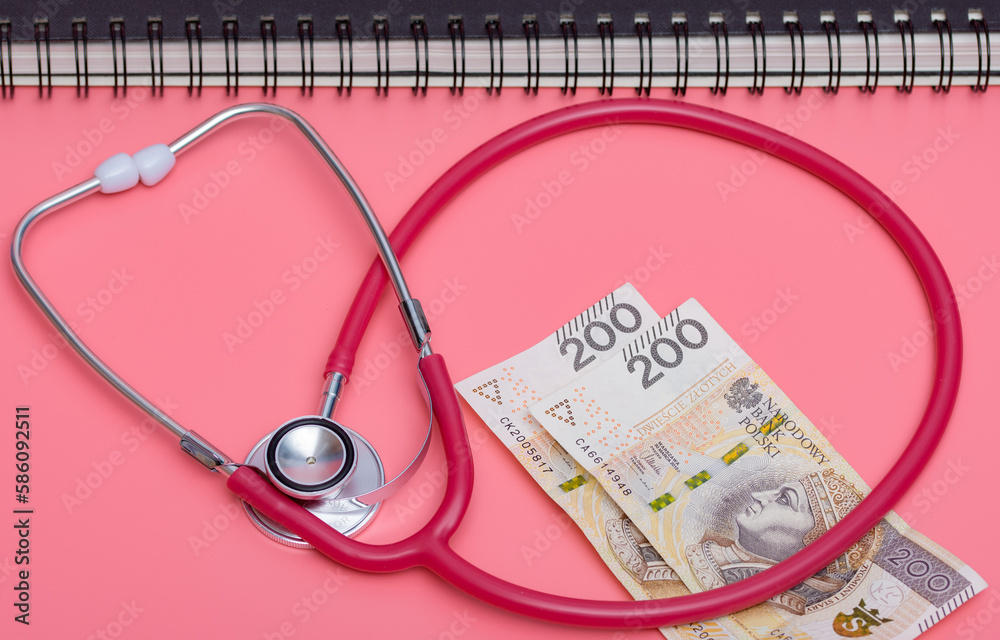 Stetoskop medyczny j polskie banknoty na różowym tle, z tyłu terminarz w formie kołonotatnika  - obrazy, fototapety, plakaty 