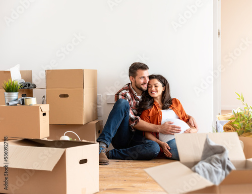 Beautiful young couple expecting a baby just moved into an empty apartment, sitting among cardboard boxes making plans for the future. New beginnings