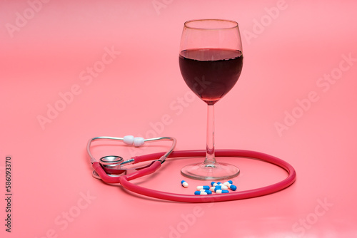 Kieliszek z czerwonym winem i stetoskopem medycznym na różowym tle