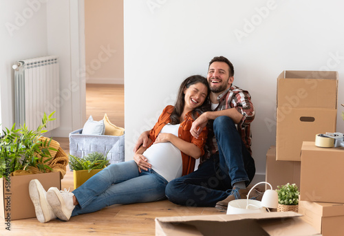 Beautiful young couple expecting a baby just moved into an empty apartment, sitting among cardboard boxes making plans for the future. New beginnings
