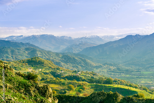 picturesque view in a green mountain valley among slopes and hills with sunny plantations on a rocky plato and nice cloudy sunset on background