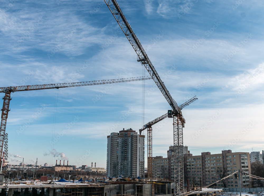 Construction cranes at a construction site in the city against the blue sky. The concept of building a new area. Construction of a new building. Construction cranes at a construction site in the city against the blue sky. The concept of building a new area. Construction of a new building.