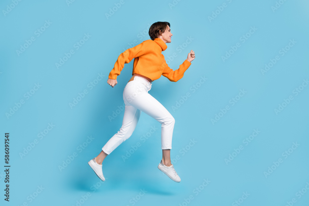 Full size photo of pretty young girl profile view running hurry speed fast dressed stylish orange look isolated on blue color background