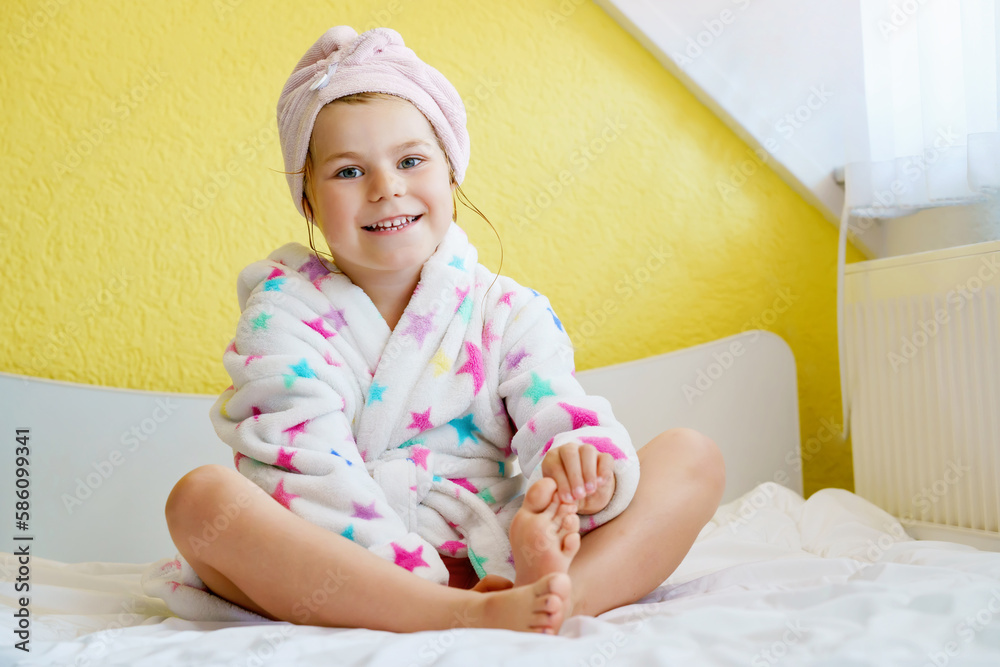 Preschool child after bath. Cute little girl with wet curly hair wearing a bathrobe and head towel sitting on bed . Bathroom textile for babies and children. Preschool child after bath. Cute little girl with wet curly hair wearing a bathrobe and head towel sitting on bed . Bathroom textile for babies and children.