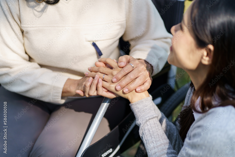 Obraz premium Family relationship Asian senior woman in wheelchair with happy daughter holding caregiver for a hand while spending time together