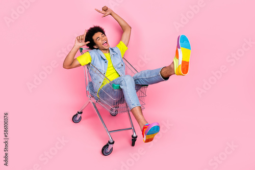 Full length photo of positive glad crazy man wear bright stylish clothes sitting cart have fun low prices isolated on pink color background