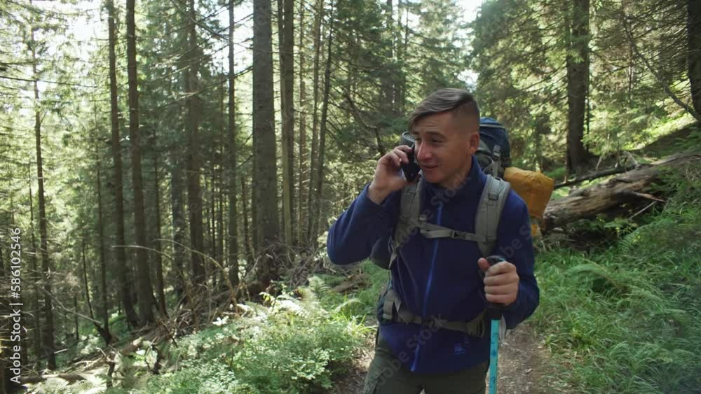 A man with a backpack, on a hike, walks through the forest and talks on the phone. Calling friends while walking. A mobile network appeared during the trip. Outdoor recreation, summer. 4k A man with a backpack, on a hike, walks through the forest and talks on the phone. Calling friends while walking. A mobile network appeared during the trip. Outdoor recreation, summer. 4k
