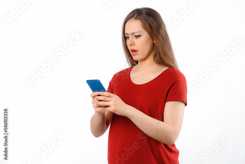 Portrait of lovely young woman using mobile phone, texting message, watching in smartphone with amazed face, standing over white background