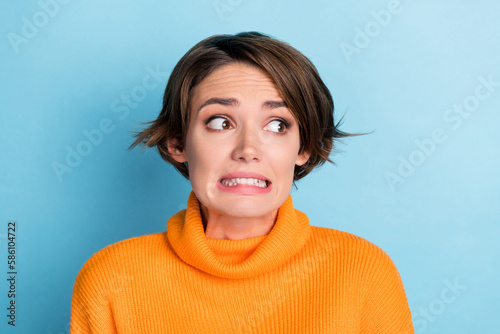 Photo of terrified anxious girl grinning teeth look empty space isolated on blue color background