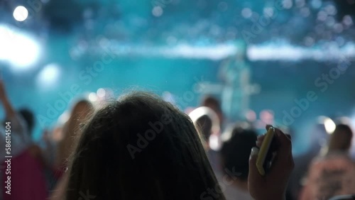 People dancing in nightclub. The girl dances inside the concert venue with her hands up. Background blurred lights.