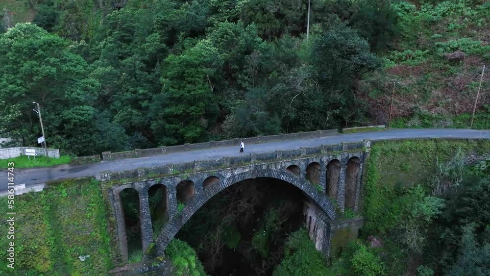 Aerial ascent of woman walking on stone bridge amongst forest, Madiera, Portugal Aerial ascent of woman walking on stone bridge amongst forest, Madiera, Portugal