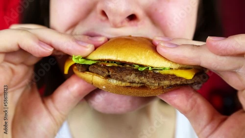 Hungry young woman biting and chewing cheeseburger with bun, meat, cheese and lettuce for lunch close up. Female mouth eating fast food