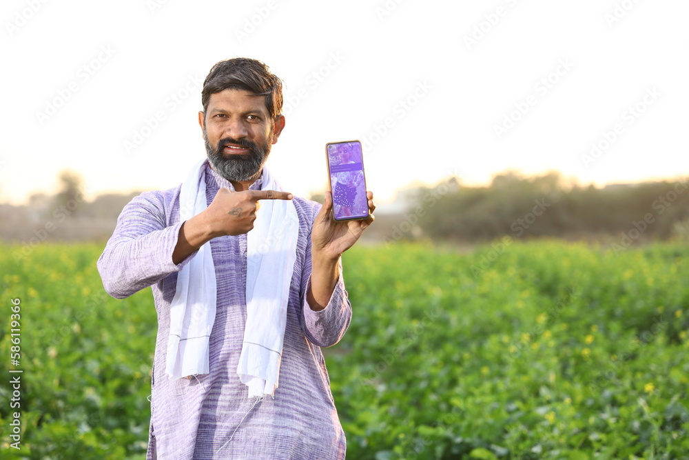 Happy rural Indian farmer pointing at the screen of his smart phone, showing his mobile phone's screen while looking at the camera . Happy rural Indian farmer pointing at the screen of his smart phone, showing his mobile phone's screen while looking at the camera .