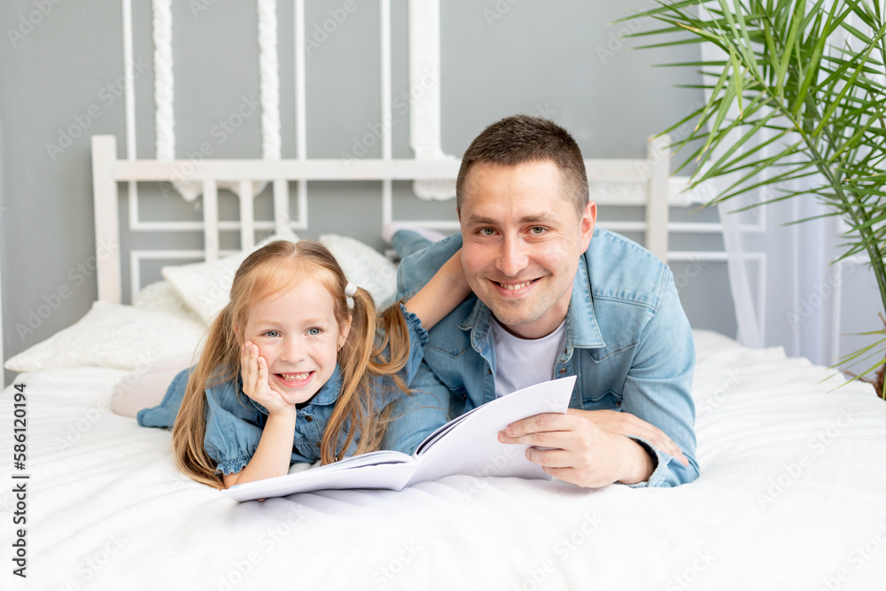 Obraz premium the father reads a book or studies with the daughter's child before going to bed or has fun