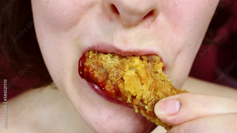 Woman eating a takeaway fried chicken wing from fast food cafe with a mouth and teeth close up Woman eating a takeaway fried chicken wing from fast food cafe with a mouth and teeth close up