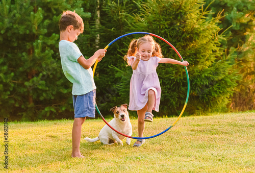 Children playing with pet dog jumping through hula hoop photo