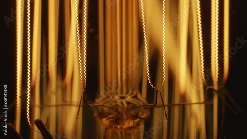 Close-up view of vintage light bulb with orange filament spiral light pulsing on black background.