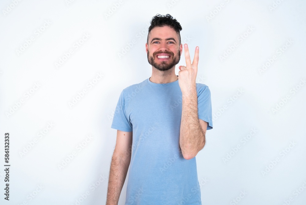 Young caucasian man wearing blue T-shirt over white background smiling and looking friendly, showing number two or second with hand forward, counting down Young caucasian man wearing blue T-shirt over white background smiling and looking friendly, showing number two or second with hand forward, counting down