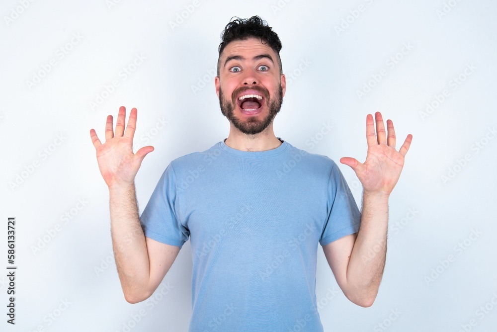 Fototapeta premium Delighted positive Young caucasian man wearing blue T-shirt over white background opens mouth and arms palms up after having great result