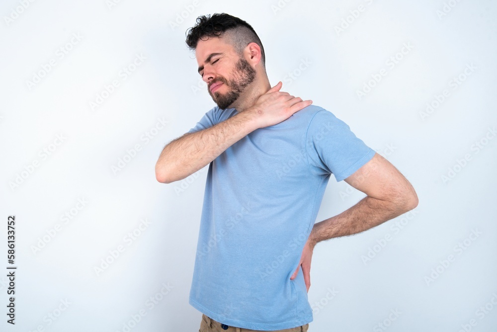 Young caucasian man wearing blue T-shirt over white background got back pain Young caucasian man wearing blue T-shirt over white background got back pain